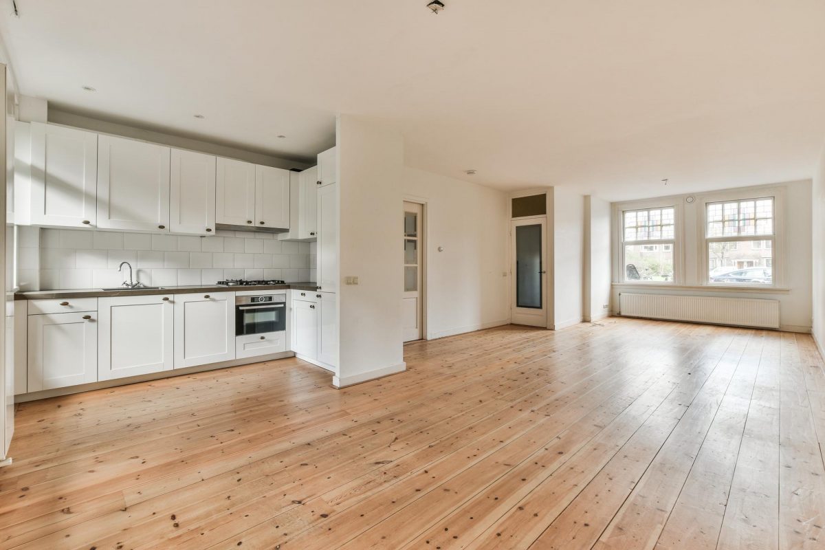 Open-concept kitchen remodel with white cabinets and wide-plank wood flooring, showing poor definition between kitchen and living space