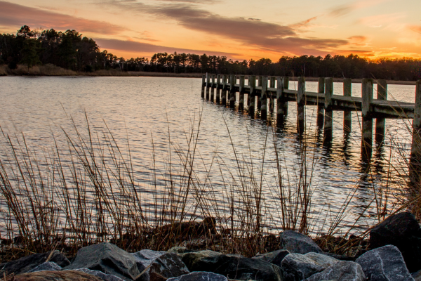 A wooden pier extending into the water at sunset on the Maryland Shore, perfect for homeowners looking to build modular coastal retreats.